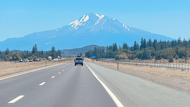 A freeway with a vehicle  driving toward a looming mount shasta